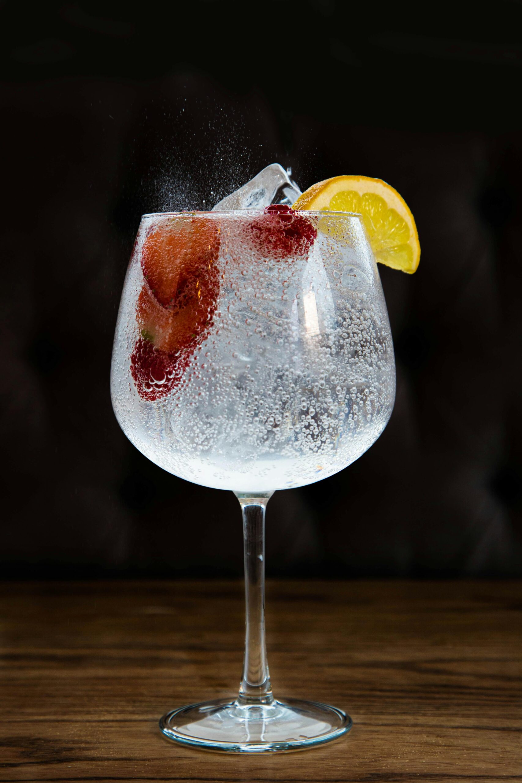 A refreshing gin and tonic with lemon and strawberries served in a glass with ice.