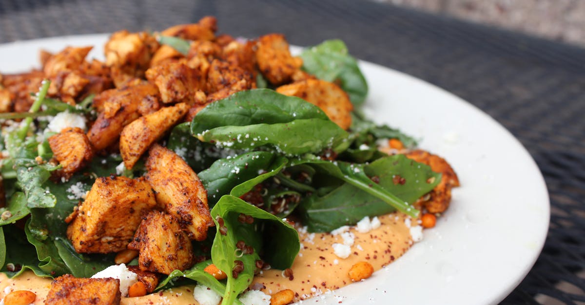 Delicious chicken salad with spinach, feta cheese, and creamy sauce on a white plate.